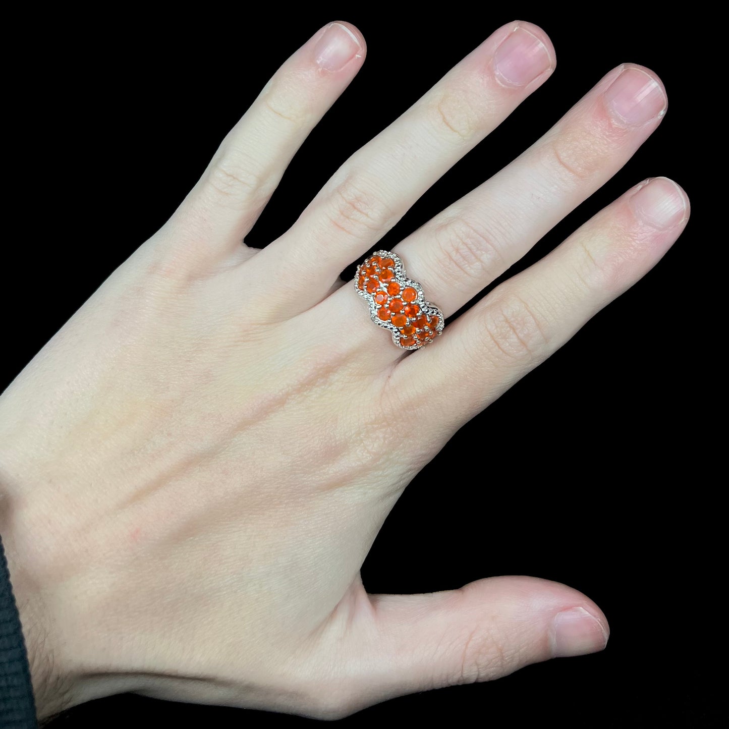 Hand wearing a sterling silver Mexican fire opal cluster ring with two diamond accents against a black background.