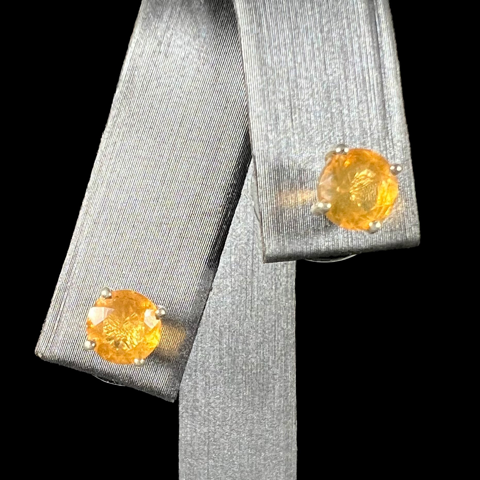 A pair of Mexican fire opal stud earrings in sterling silver shown from the front against a black background.