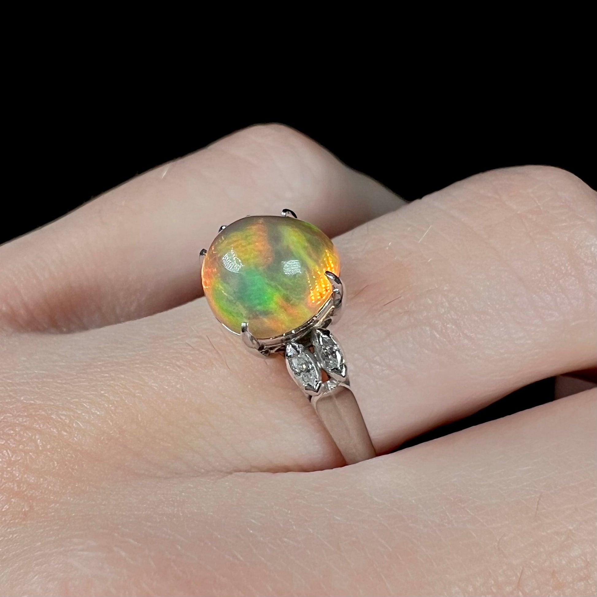 Angled close-up of a Mexican fire opal engagement ring worn on a finger, featuring a 2.28ct round opal with vivid red and green fire in platinum.