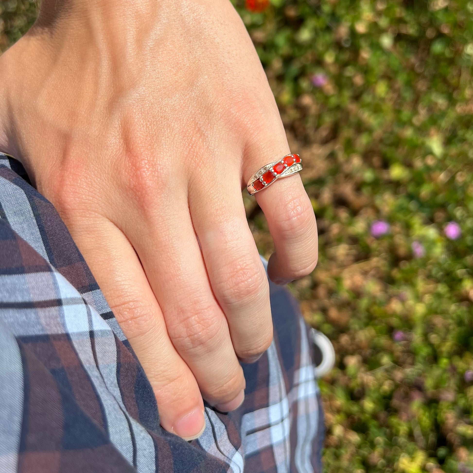 Hand placed on hip wearing Mexican fire opal ring in natural light against a blurred green background.