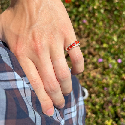 Hand placed on hip wearing Mexican fire opal ring in natural light against a blurred green background.