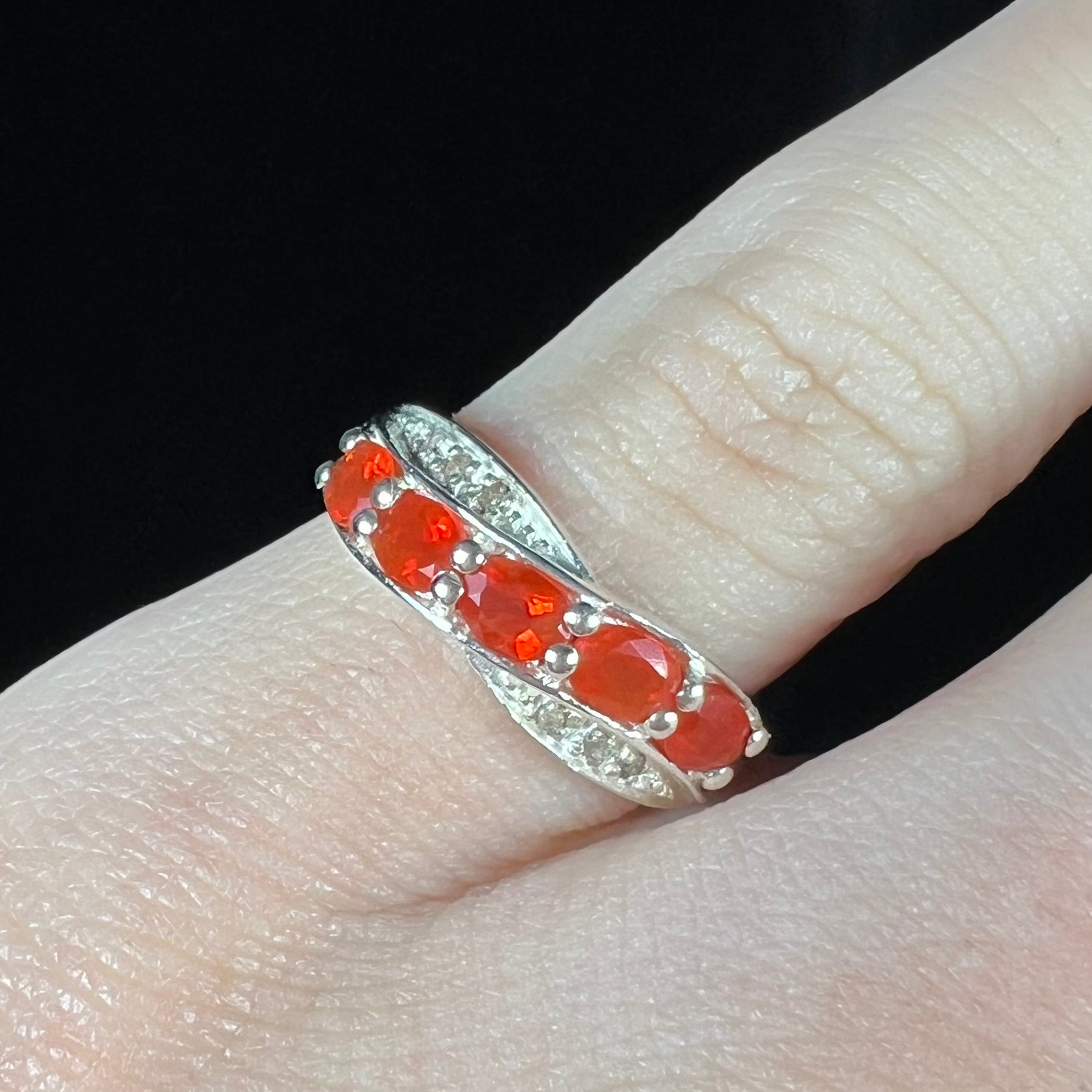 Close-up of silver ring with orange Mexican fire opal gemstones worn on a finger against black background.