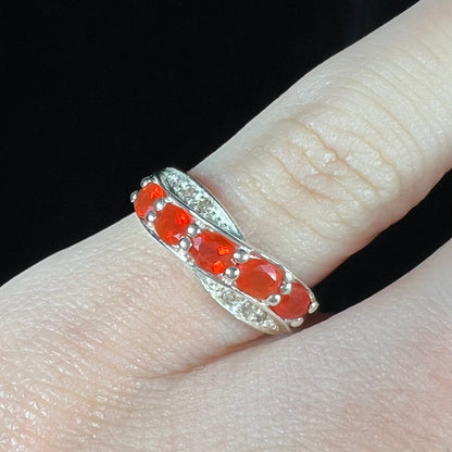 Close-up of silver ring with orange Mexican fire opal gemstones worn on a finger against black background.