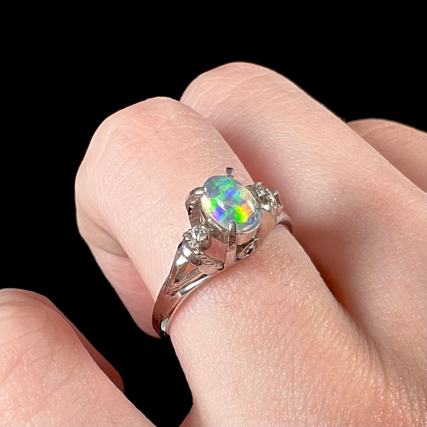 A jelly opal and diamond engagement ring on a finger.  The ring has two diamond accents.