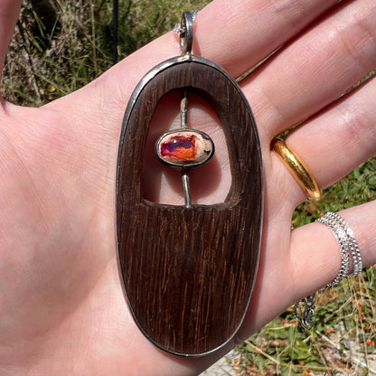 Close-up of a Mexican matrix opal and hand-carved wood pendant in sterling silver, held in a hand in natural sunlight.