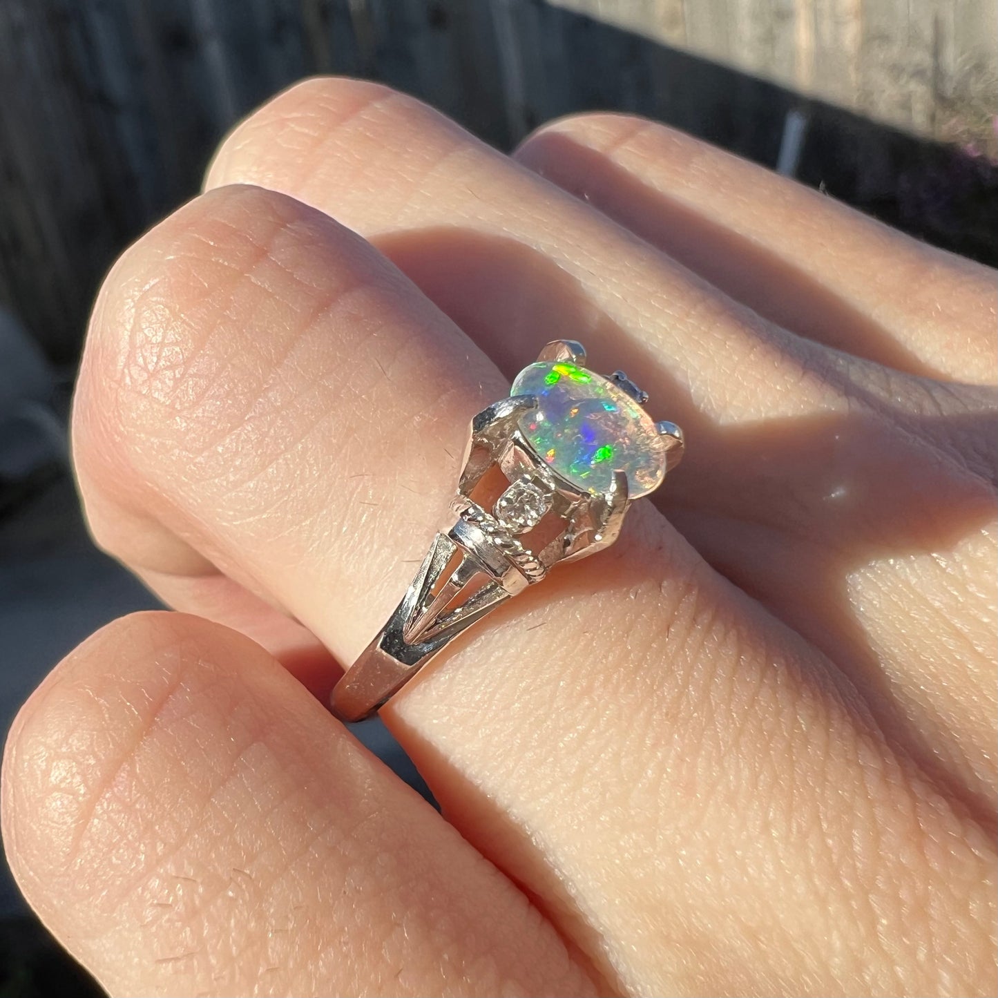 A dainty platinum jelly opal ring with diamonds worn on a finger in natural sunlight.