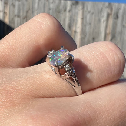 A dainty Mexican jelly opal ring with diamonds worn on a finger in natural sunlight.