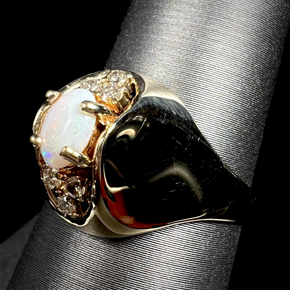Angled macro view of Mid-Century era 14k gold opal and diamond ring with a highly polished dome design, shown on ring display