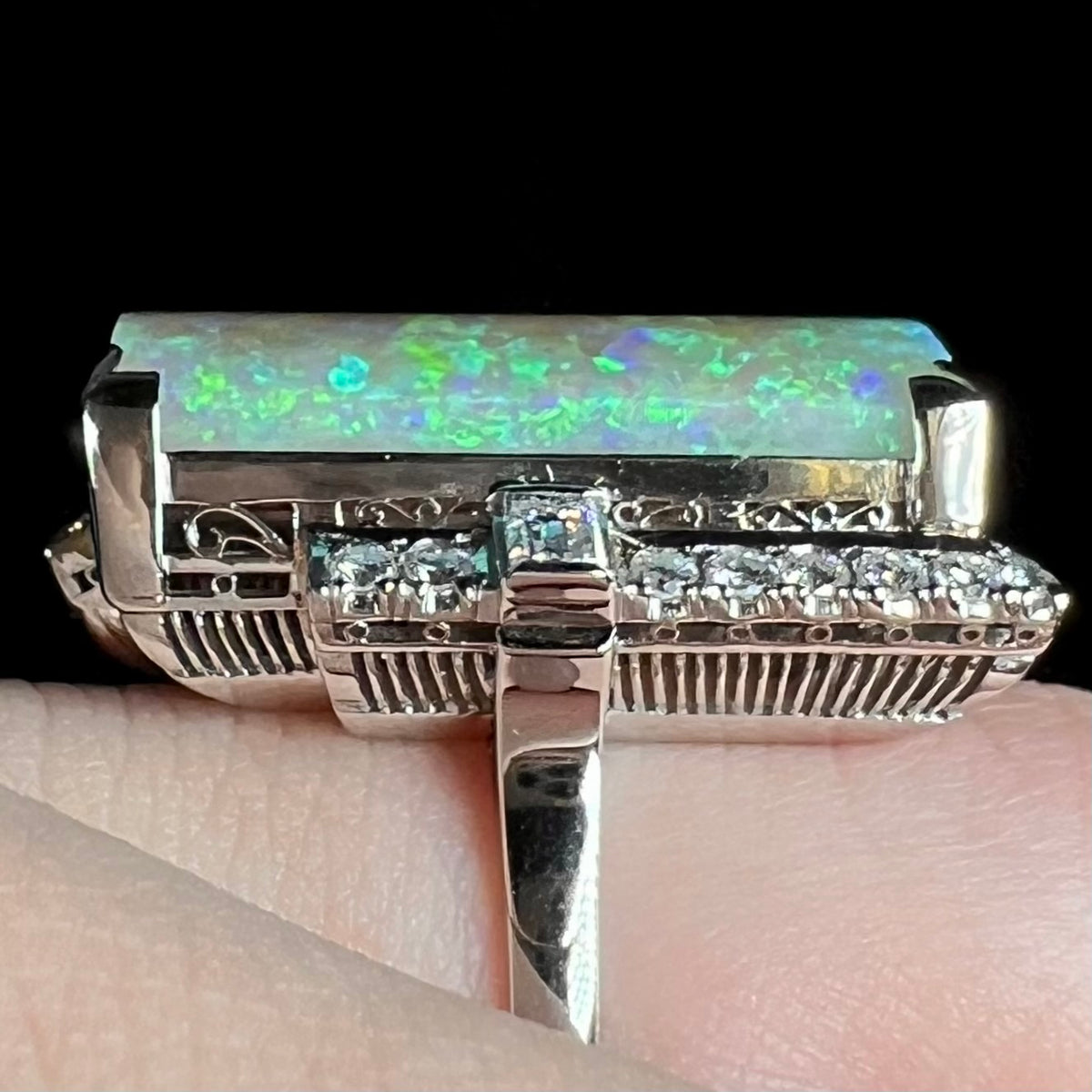 Close-up of mid-century Japanese Showa cocktail ring with intricate open platinum filigree and vertical ribbed design featuring Australian opal and diamonds, worn on finger.
