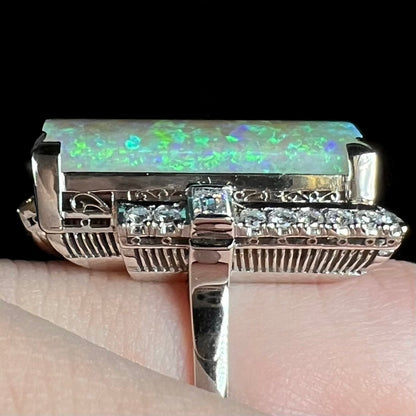 Close-up of mid-century Japanese Showa cocktail ring with intricate open platinum filigree and vertical ribbed design featuring Australian opal and diamonds, worn on finger.
