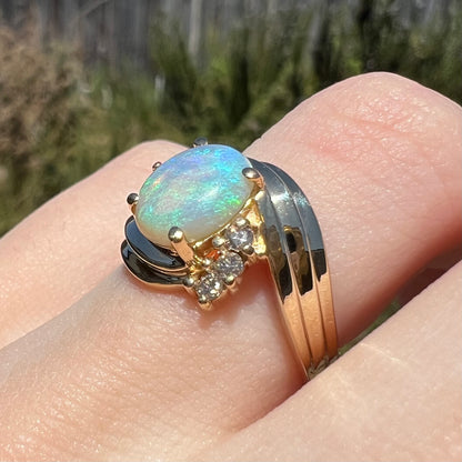 Modernist style 14k gold prong-set Australian opal and diamond ring, worn on finger in natural light