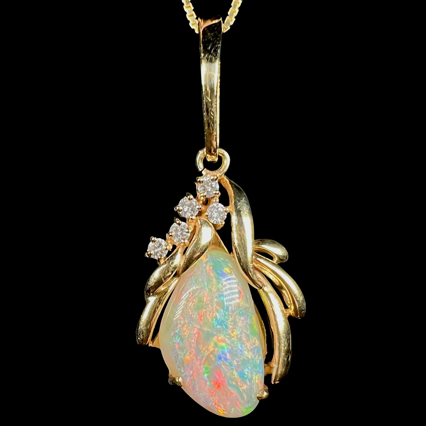 Close-up of Modernist-style 14k yellow gold Coober Pedy shell opal pendant with diamond accents, shown from the front against black background.