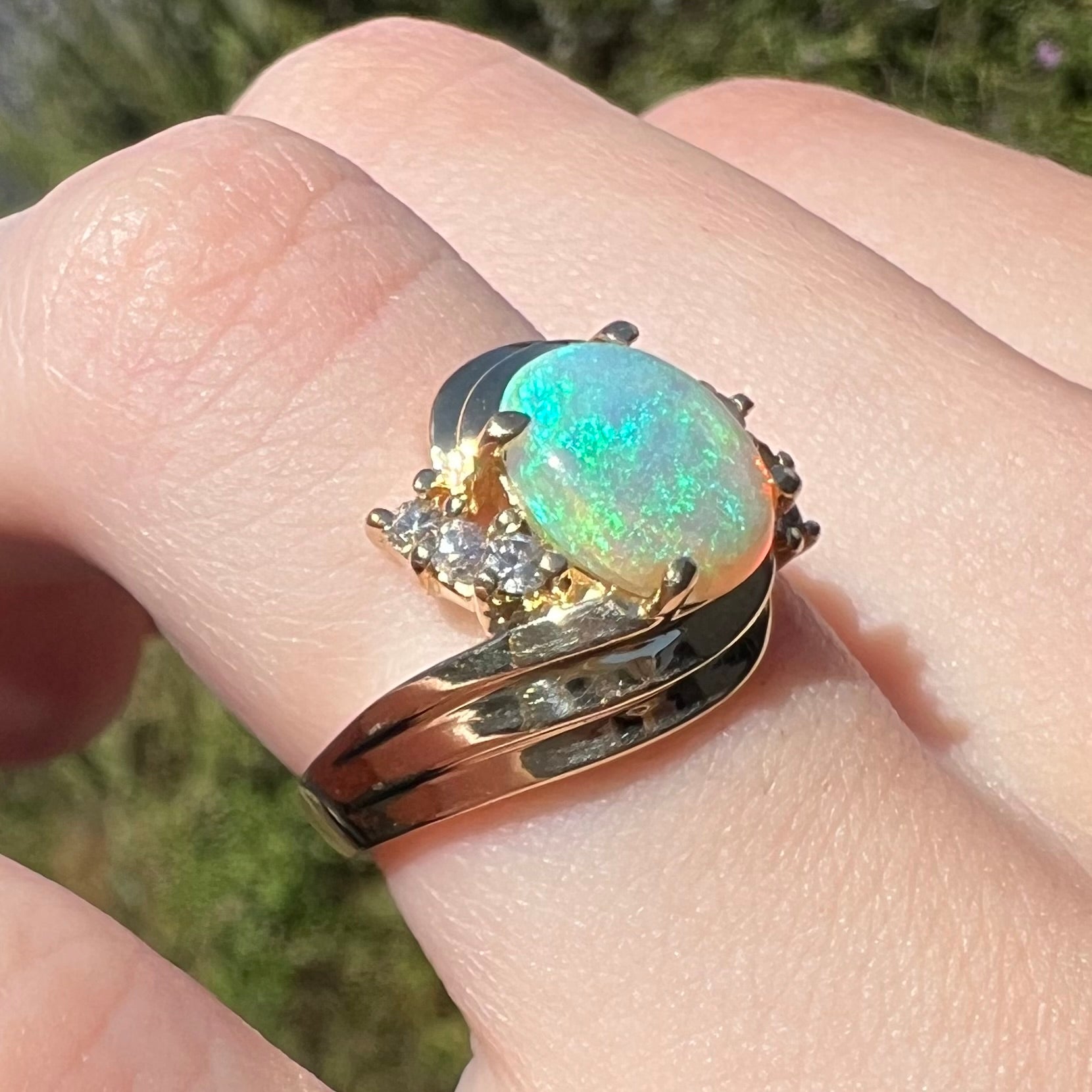 Close-up of Modernist style 14k gold ring set with diamond accents and blue-green Australian opal, worn on finger under natural light