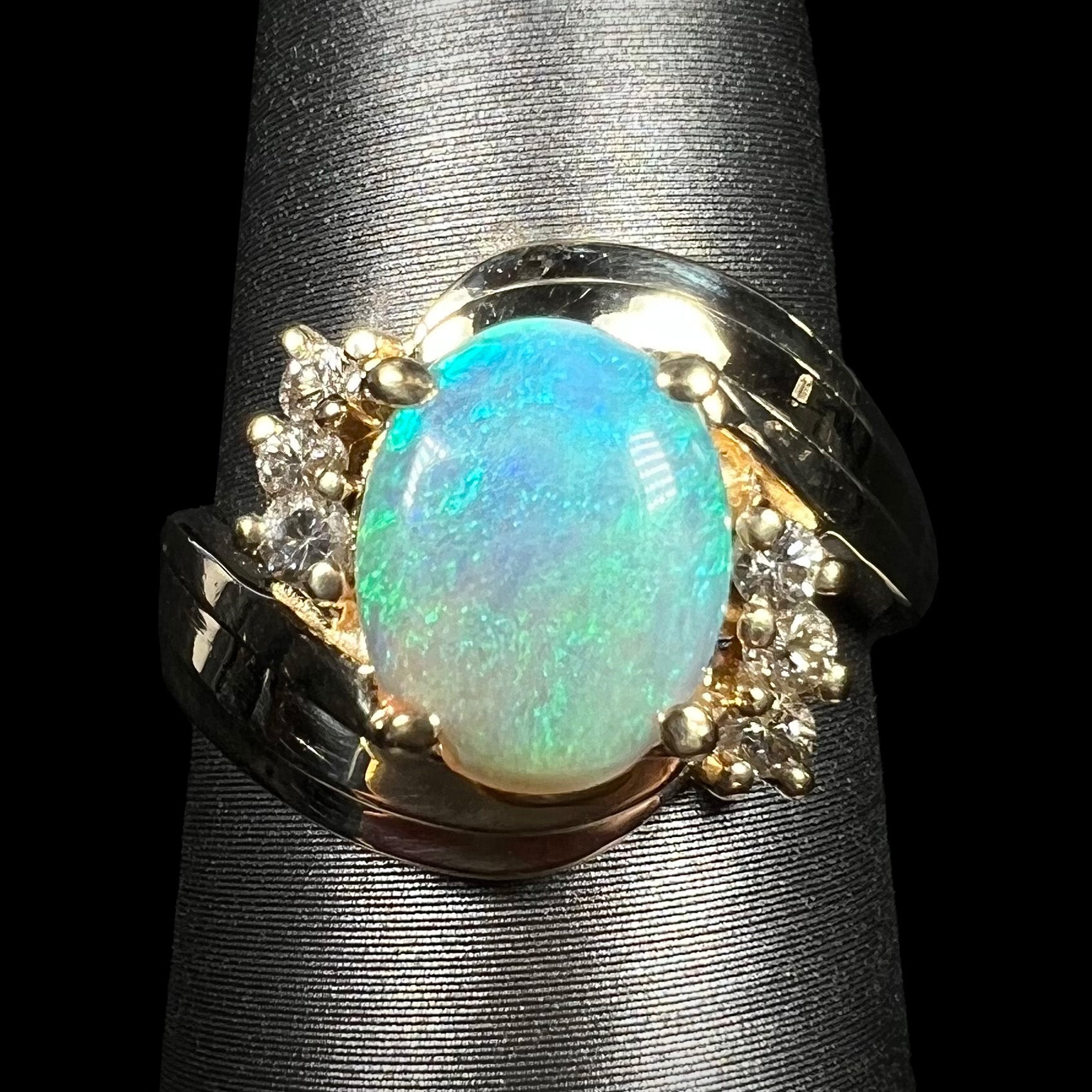Close-up of 1980s Modernist style 14k gold crystal opal and diamond ring with bypass shank design, on ring display