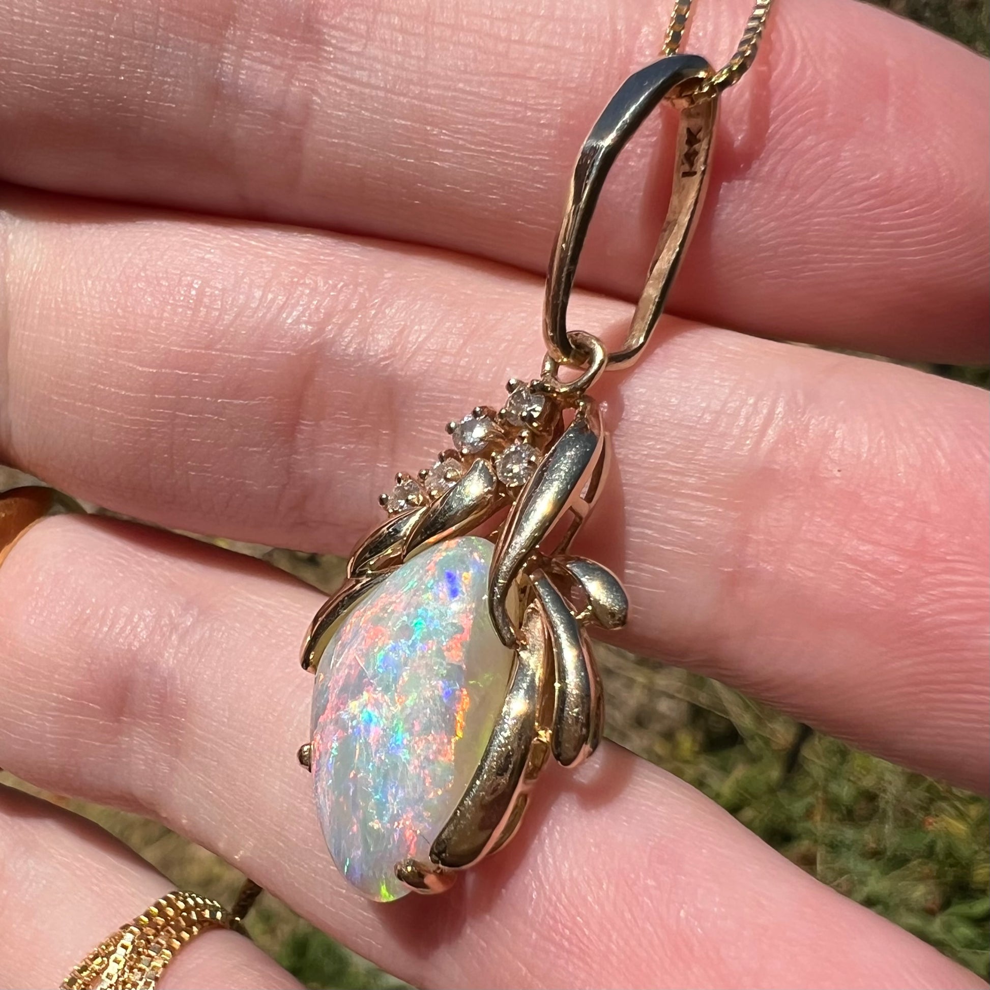 A women's Modernist-style 14k yellow gold Australian opal and diamond pendant shown close-up from an angle in natural light.