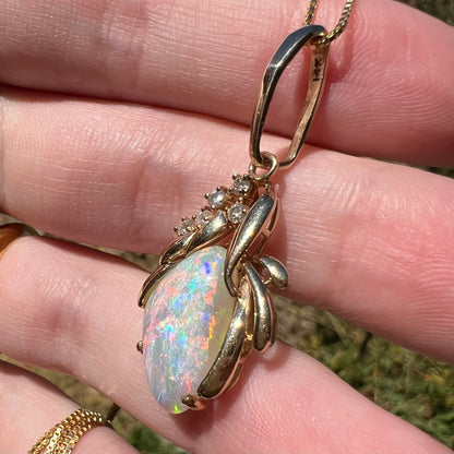 A women's Modernist-style 14k yellow gold Australian opal and diamond pendant shown close-up from an angle in natural light.