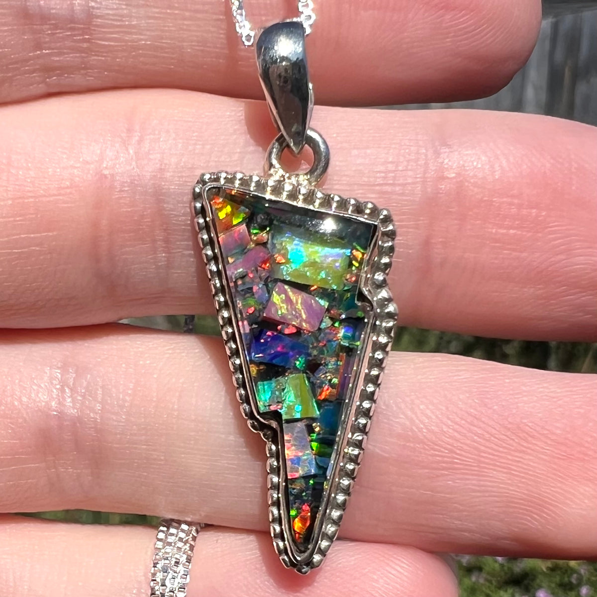 Close-up of lightning bolt-shaped mosaic opal pendant with Southwest-inspired sterling silver beaded design, held in natural sunlight.