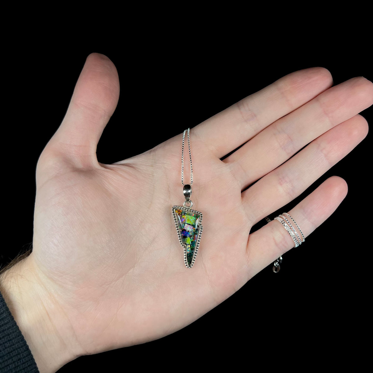 Hand holding a lab-created mosaic opal triplet necklace, shaped like a lightning bolt.