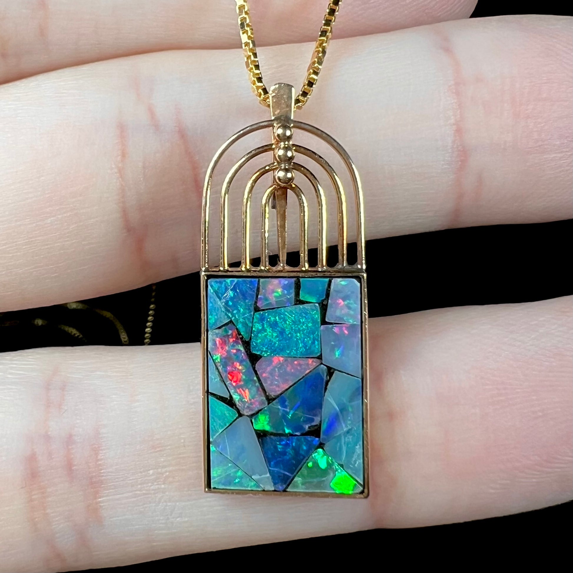 Macro shot of an 18k gold mosaic opal necklace, showing intense red flashes in the opal.