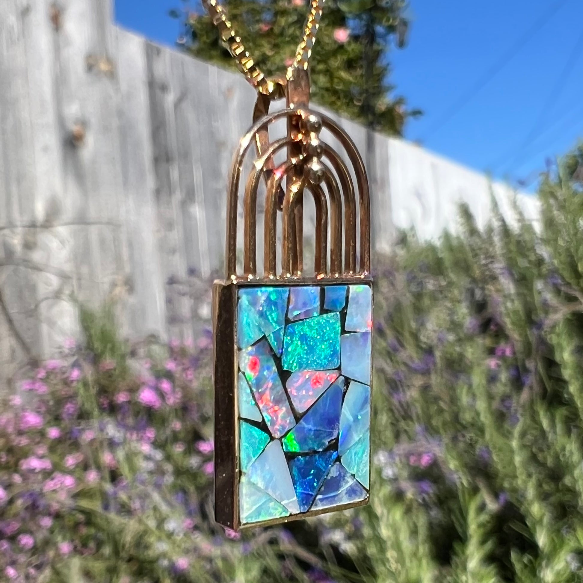 A macro view of a mosaic opal necklace outdoors at an angle, with predominantly red flashes.