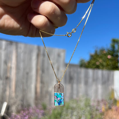 A mosaic opal necklace outdoors in sunlight, with red flashes most visible from a distance.