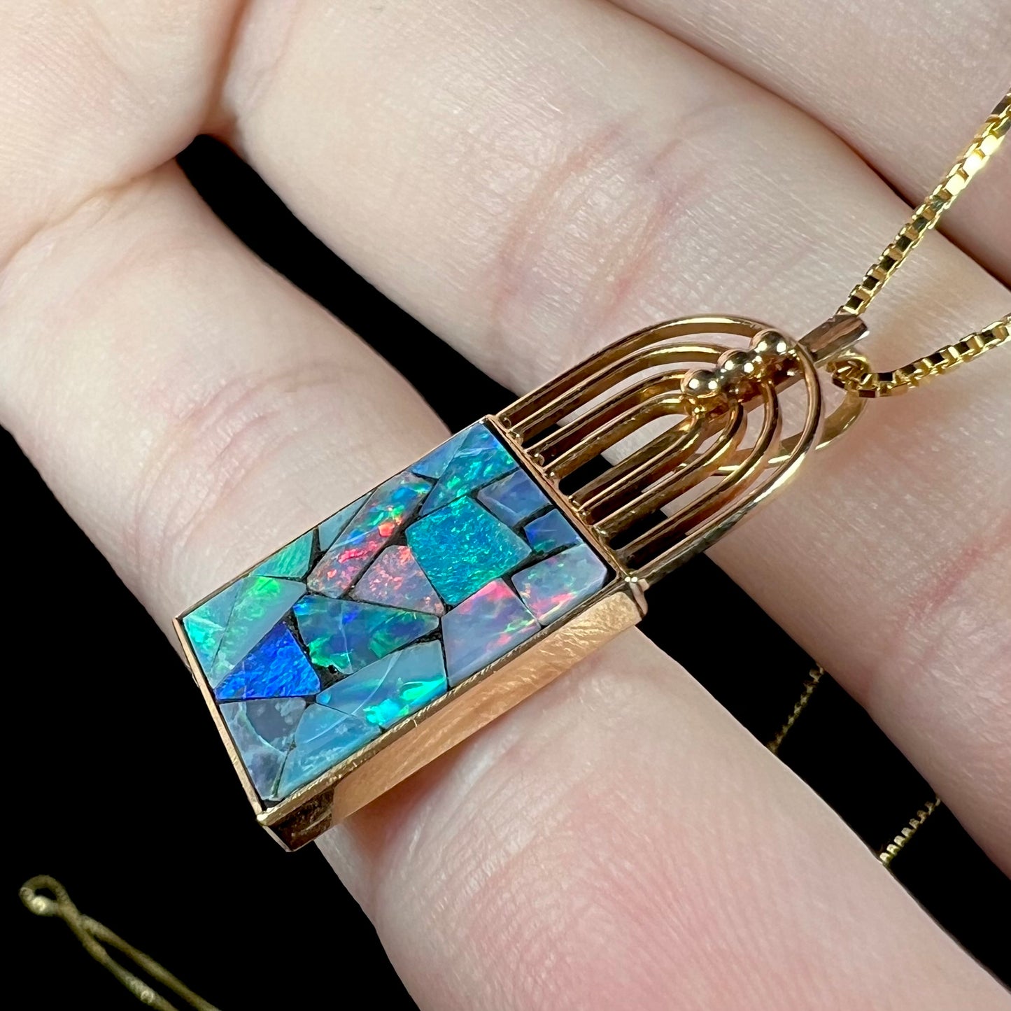 Side view of a gold mosaic opal necklace, showing blue and red flashes across the opal inlays.