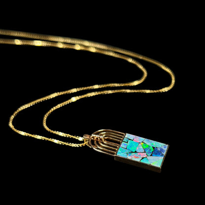  angled shot of a gold mosaic opal pendant on a black background, showing vibrant green and red color play.