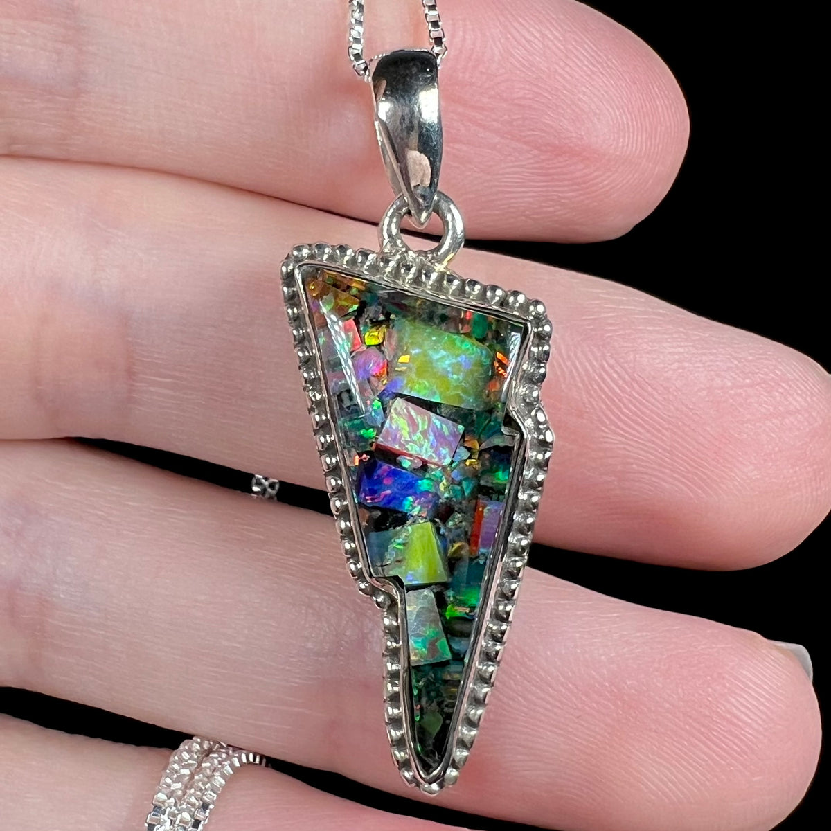 Close-up of multicolor synthetic mosaic opal pendant in sterling silver, held in hand.