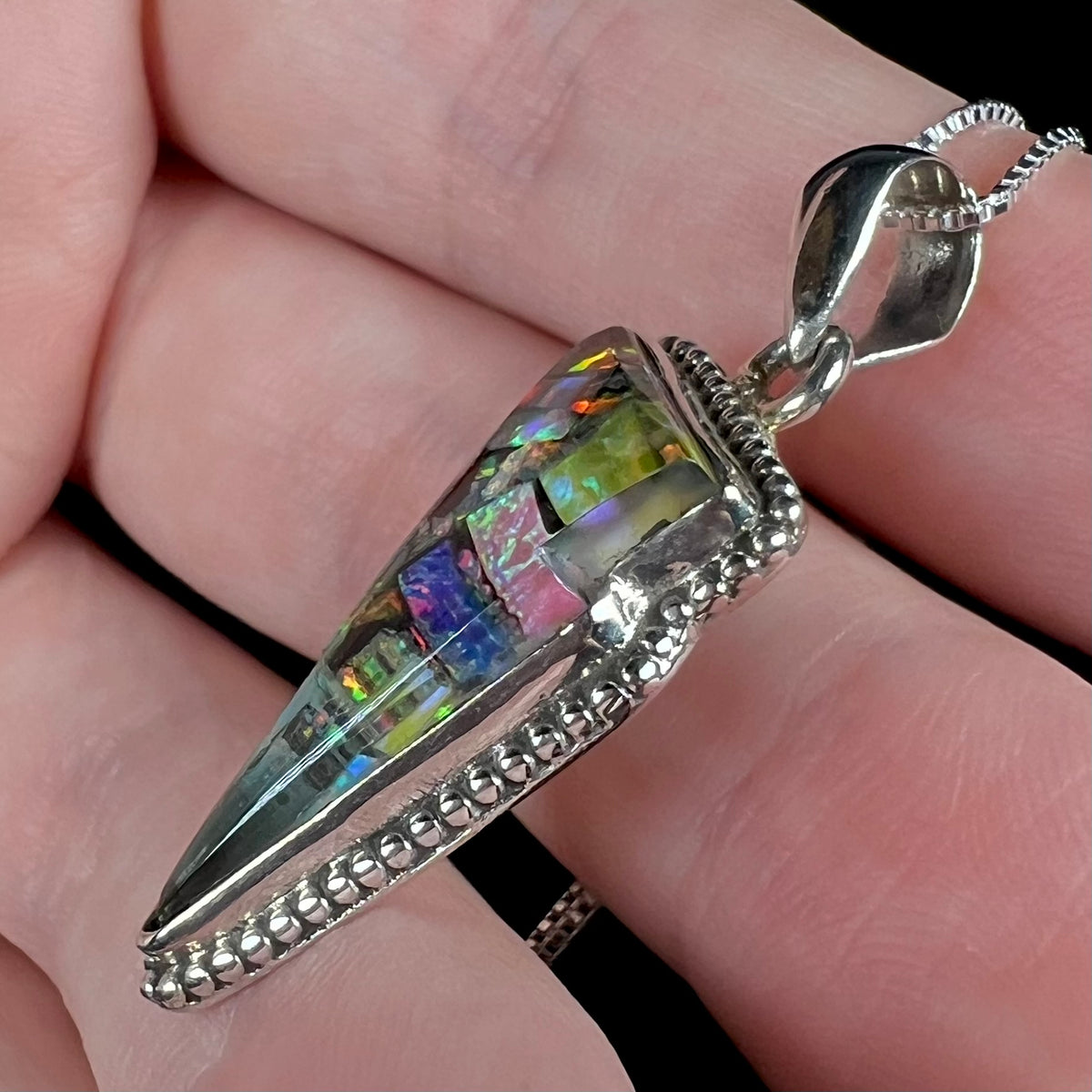 Side view of mosaic opal pendant with sterling silver beaded design showing glass cap on top of opals, held in hand.