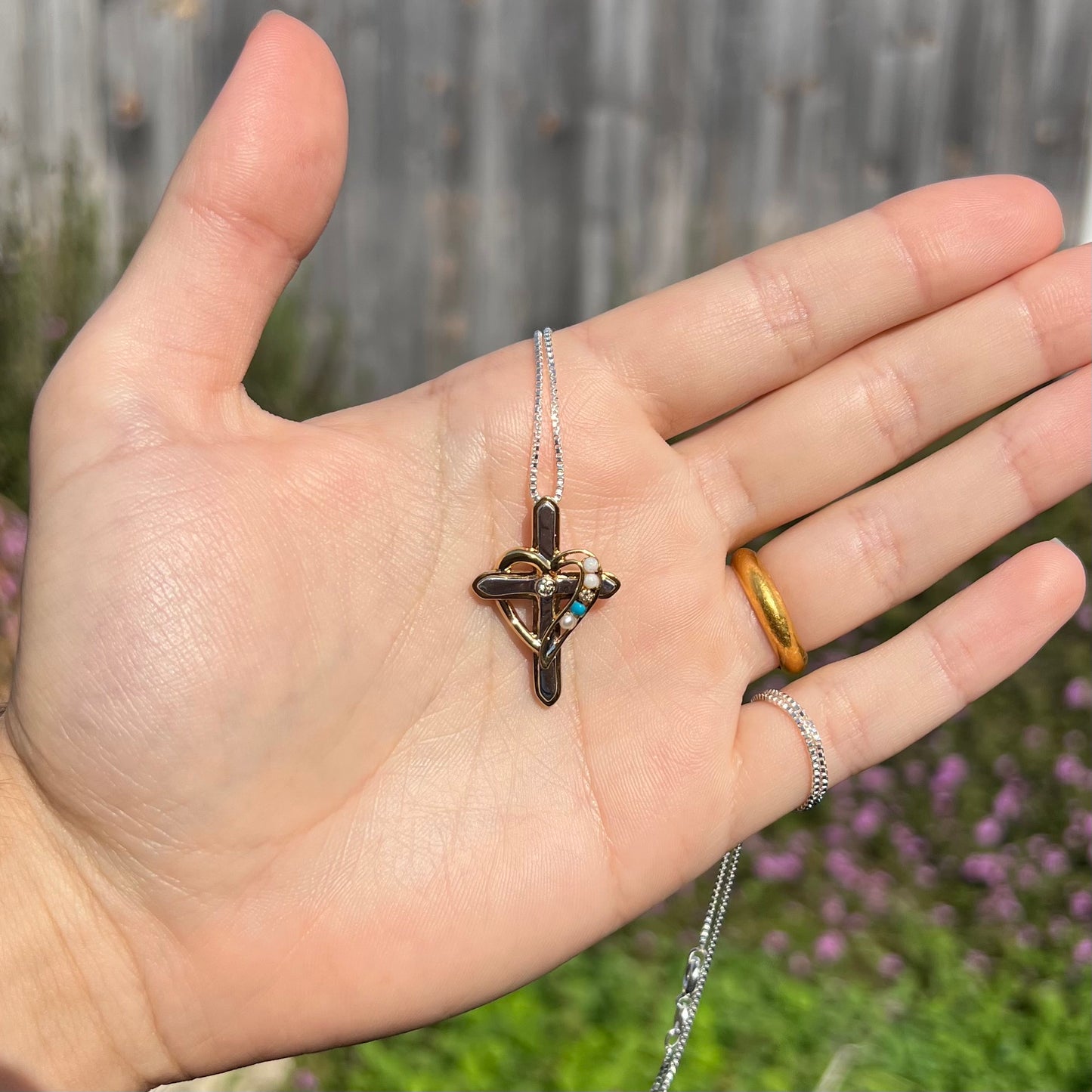 A two-tone sterling silver mother's cross necklace set with diamond, opal, turquoise, and pearl, shown in sunlight.