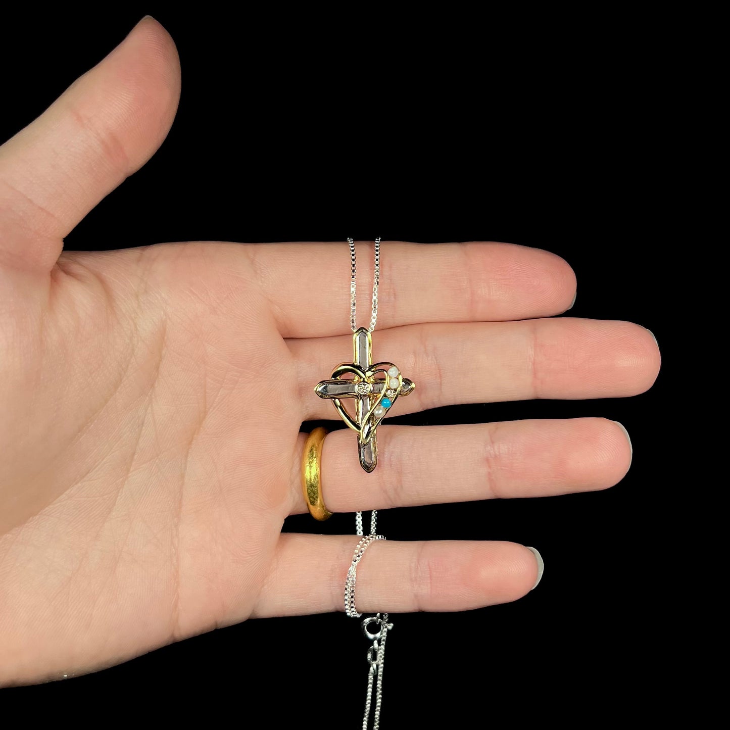 A two-tone sterling silver mother's cross necklace set with diamond, opal, turquoise, and pearl, shown in a hand.