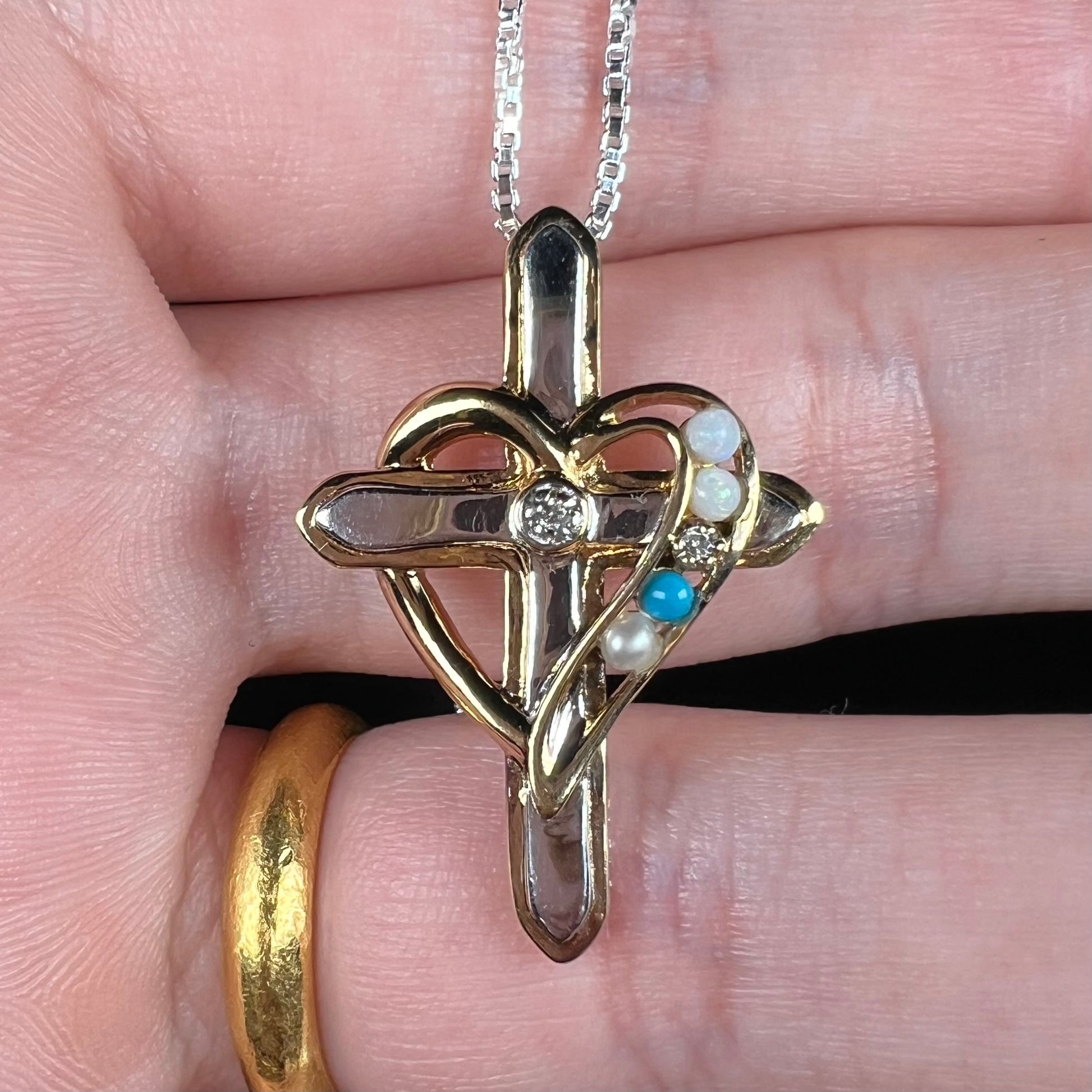 A two-tone sterling silver mother's cross necklace set with diamond, opal, turquoise, and pearl.