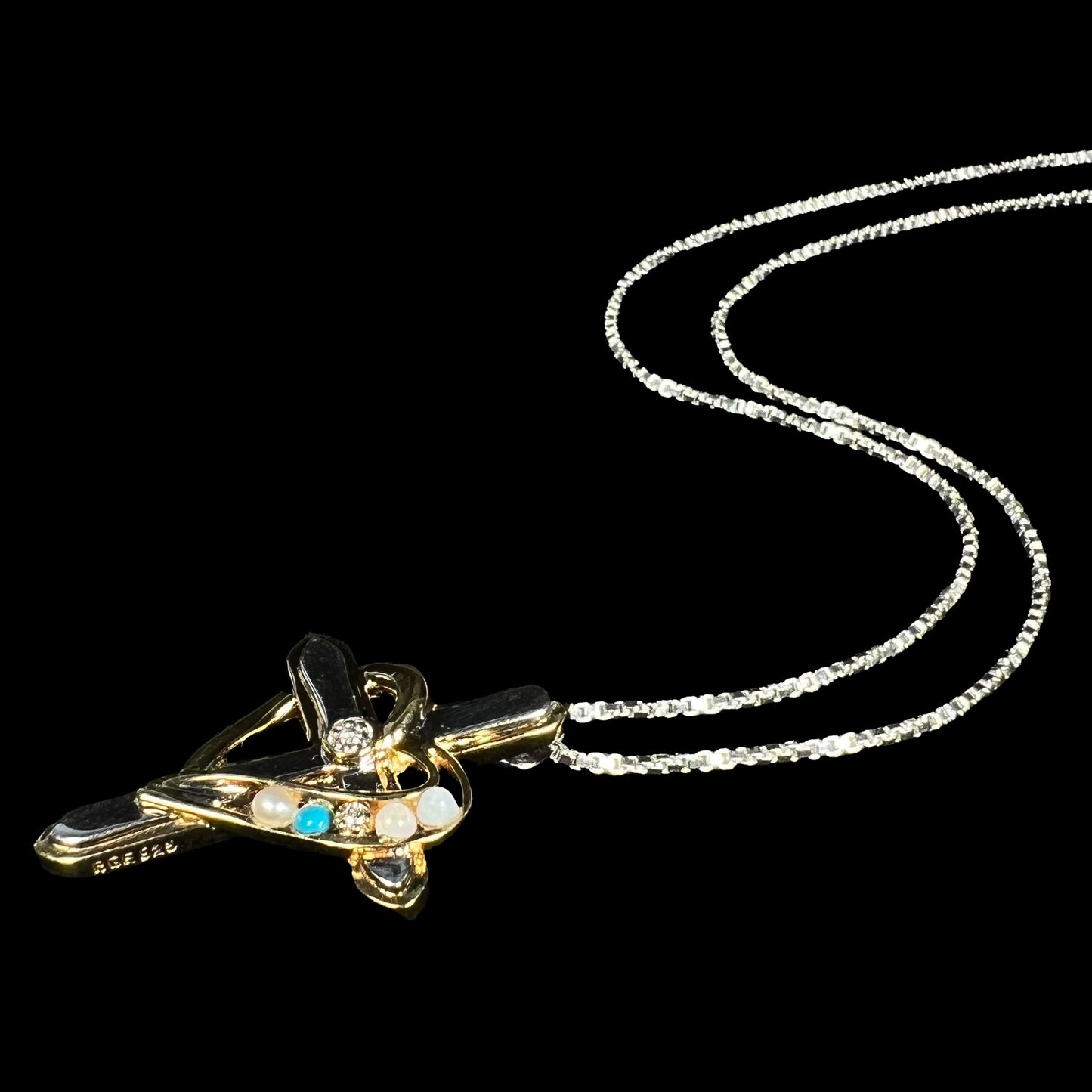 Angled view of a two-tone sterling silver mother's cross necklace set with diamond, opal, turquoise, and pearl.