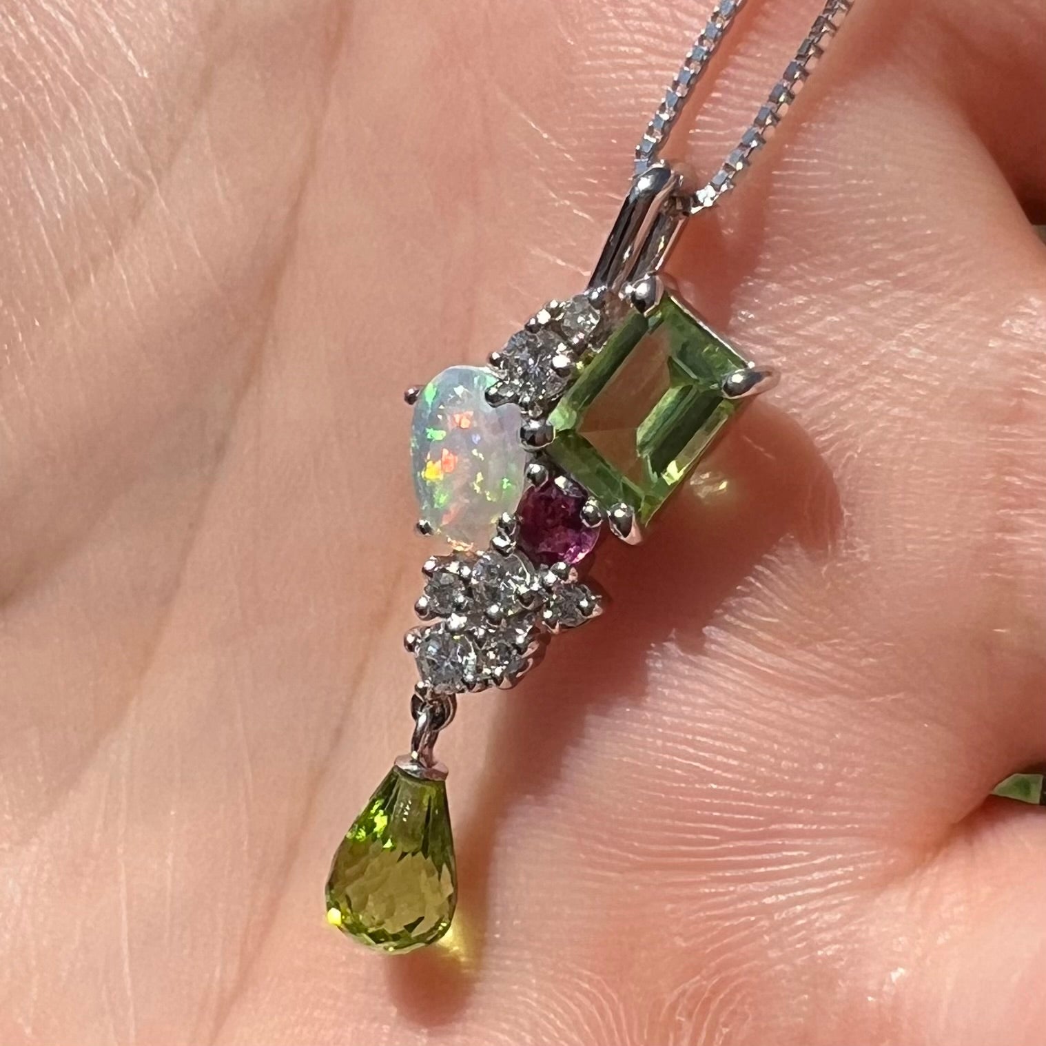 A multi-gemstone cluster pendant held in a hand at an angle in natural daylight.