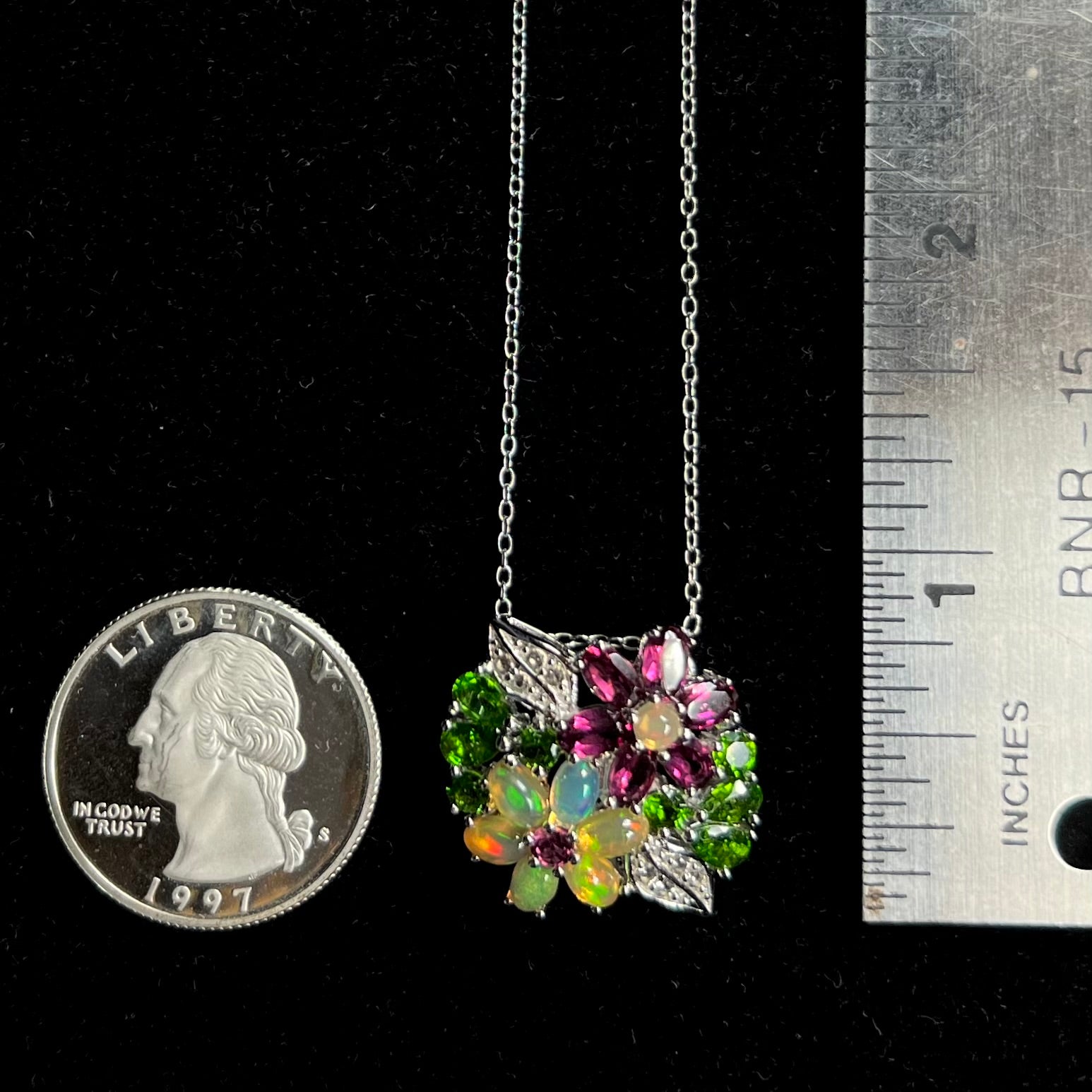 A multi-gemstone flower necklace shown next to a quarter coin and ruler.