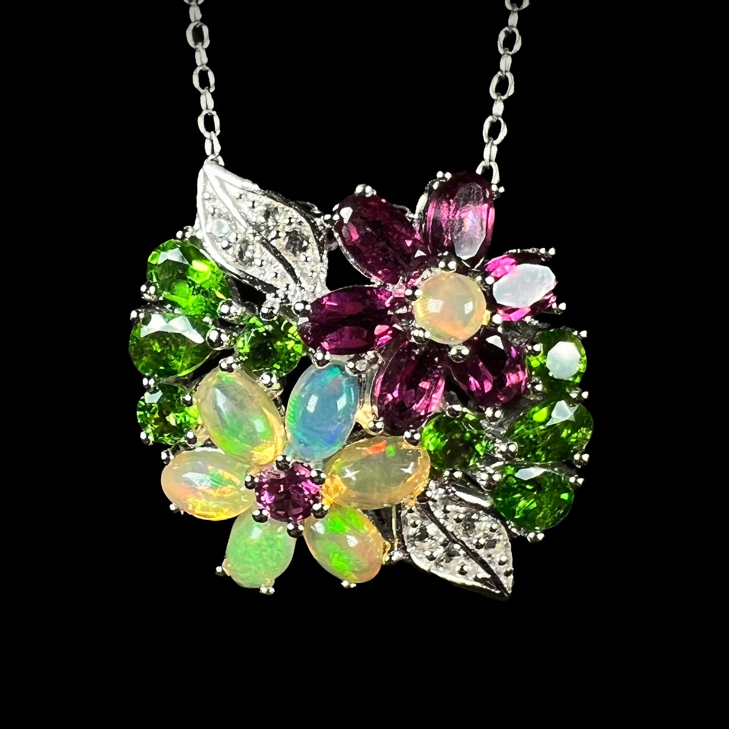 Multi-gemstone flower necklace in silver with opal and garnet, shown from the front against black background.