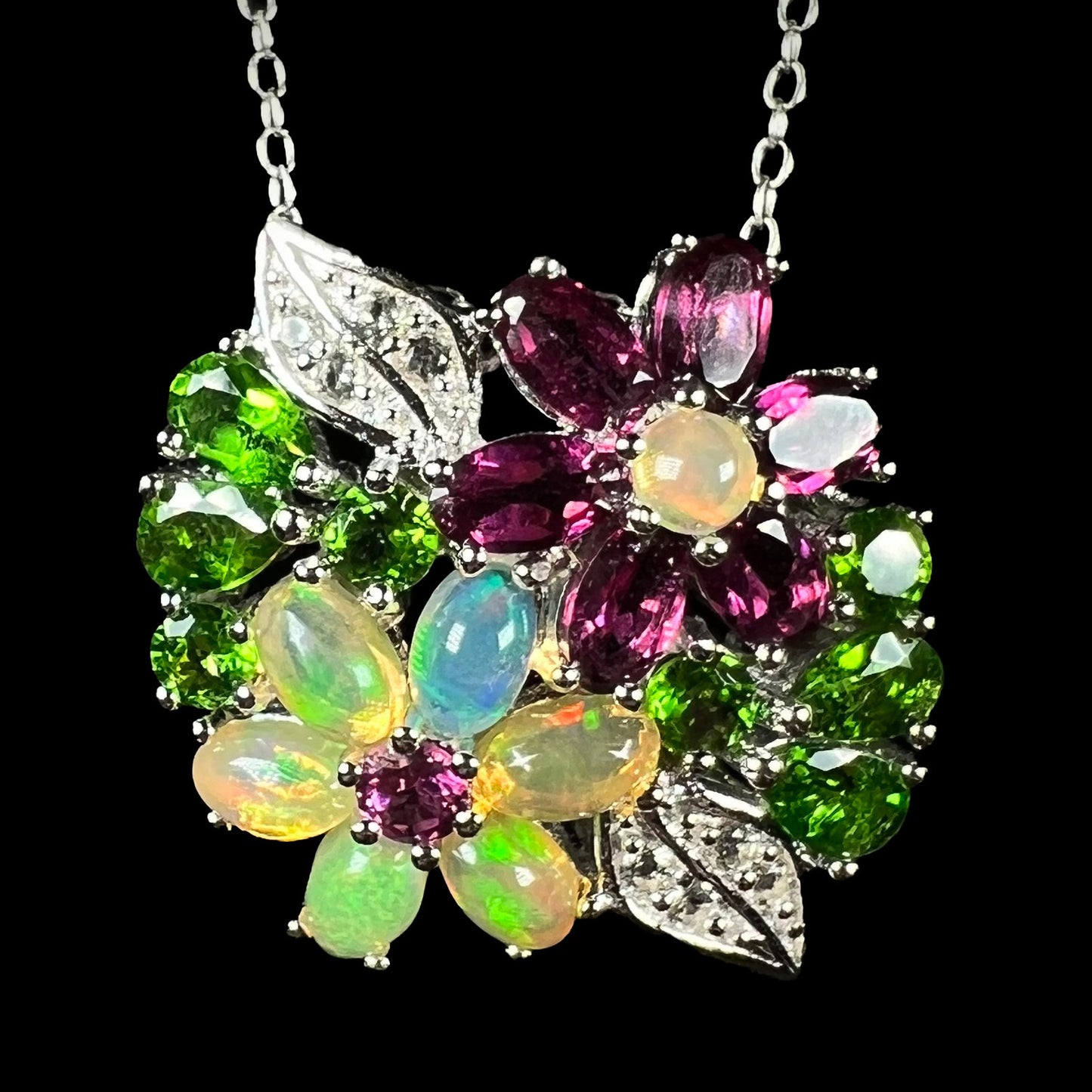 Multi-gemstone flower necklace in silver with opal and garnet, shown from the front against black background.