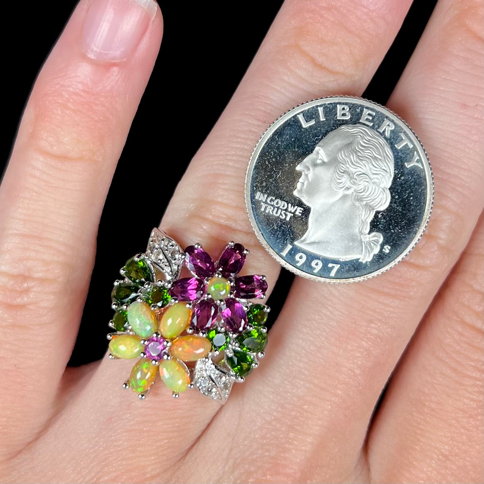 A multi-gemstone flower ring with Ethiopian opal, worn on a finger next to a 1997 quarter coin for scale.