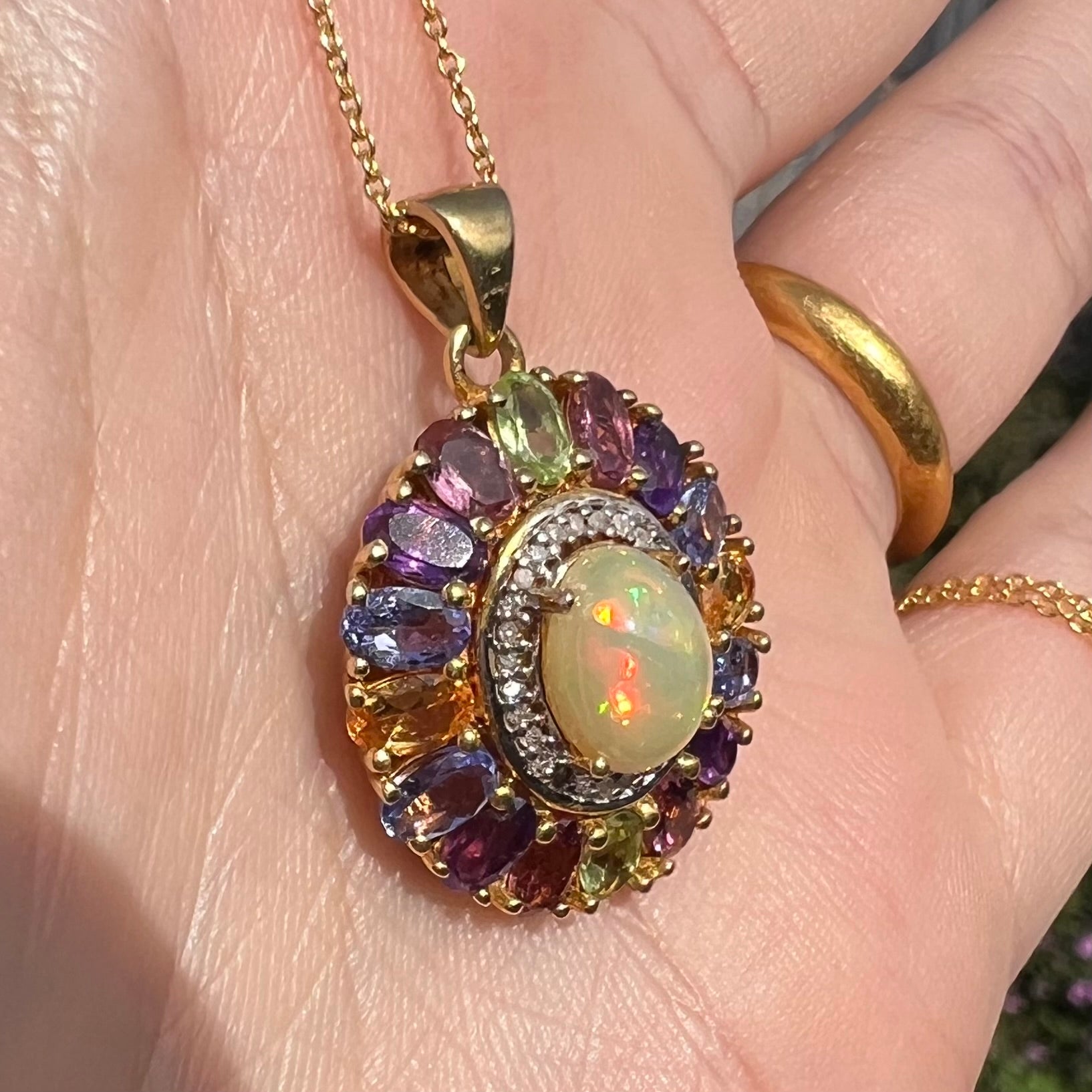 A gold plated sterling silver Ethiopian fire opal and multi-gemstone halo pendant shown from an angle.
