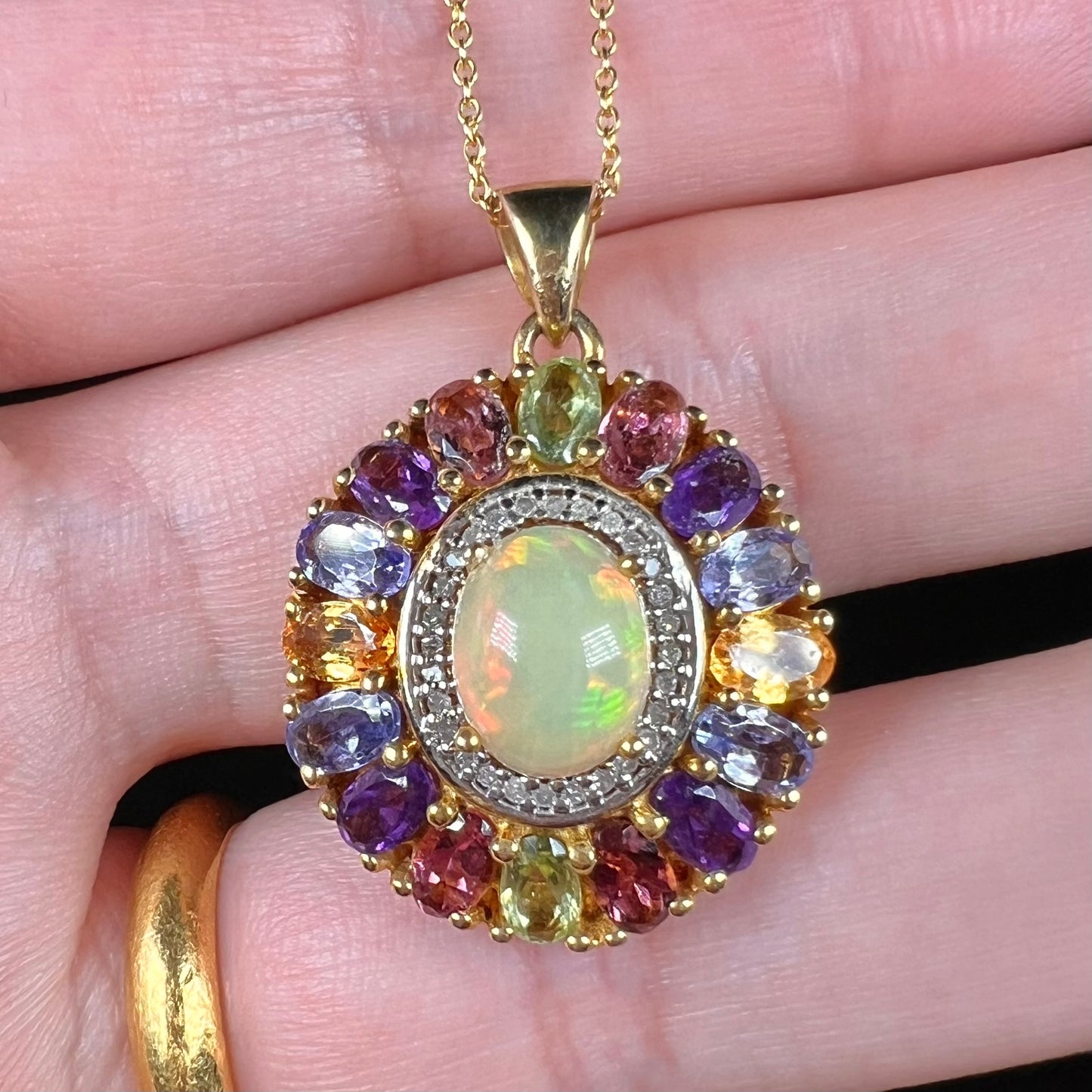 A gold plated sterling silver Ethiopian fire opal and multi-gemstone halo pendant shown close-up in a hand.