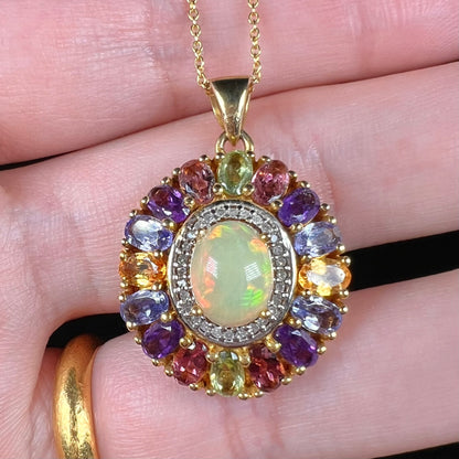 A gold plated sterling silver Ethiopian fire opal and multi-gemstone halo pendant shown close-up in a hand.