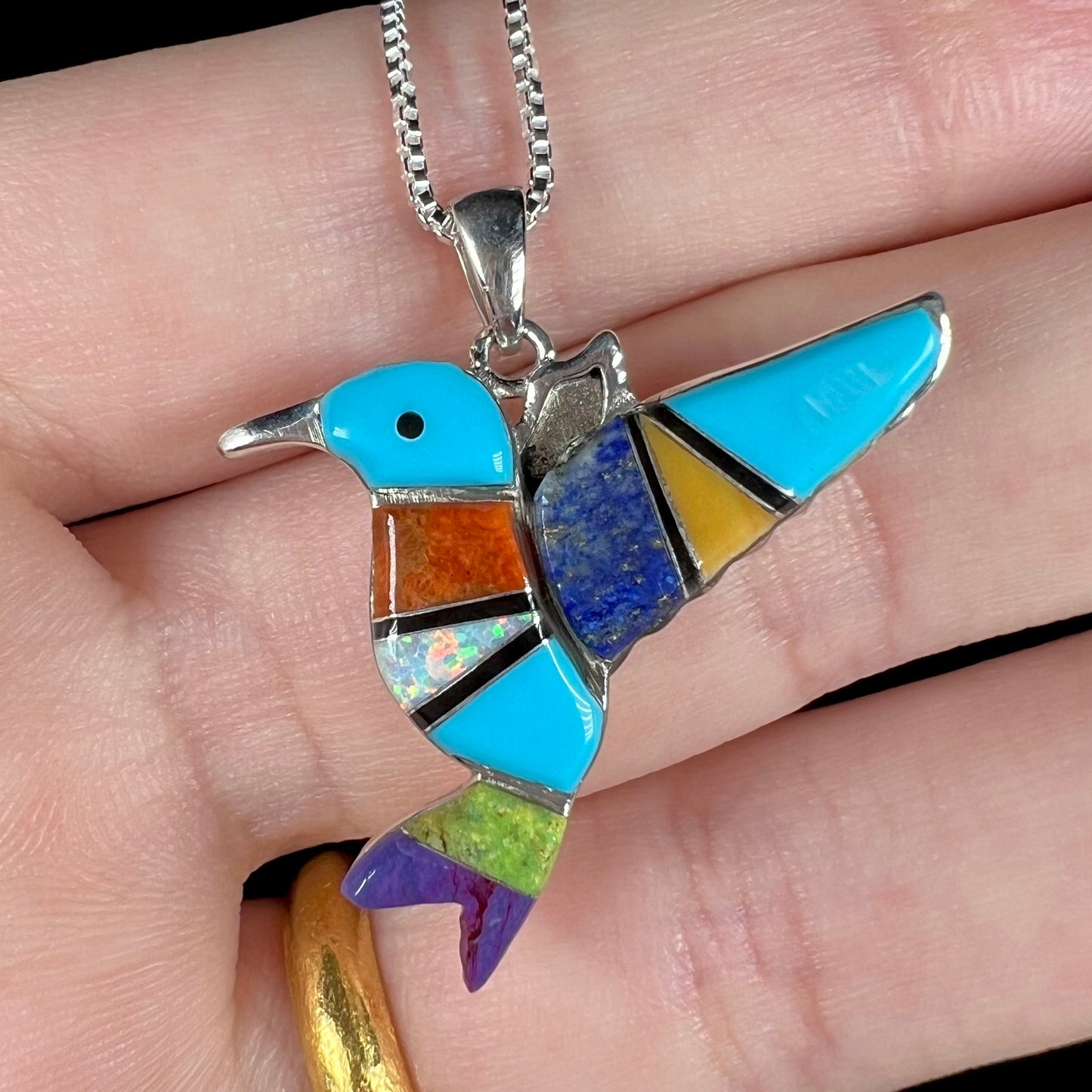 A multi-stone inlay hummingbird necklace in sterling silver, shown close-up in a hand.