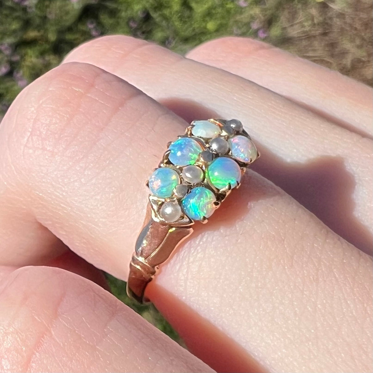 Six colorful round opals glow with greens, blues, and pink in sunlight, mounted in Victorian 9k gold multi-stone ring setting, worn on finger and viewed from angle