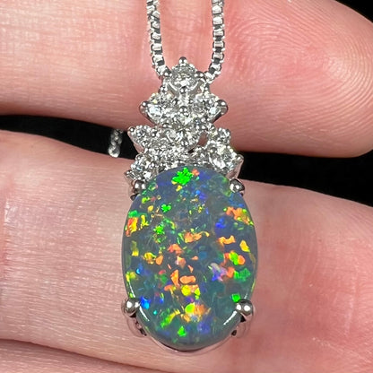 Bottom-up angled view of a multicolor Australian black opal pendant with diamond accents.  Red, orange, yellow, green, blue, and purple flashes seen across opal's surface.