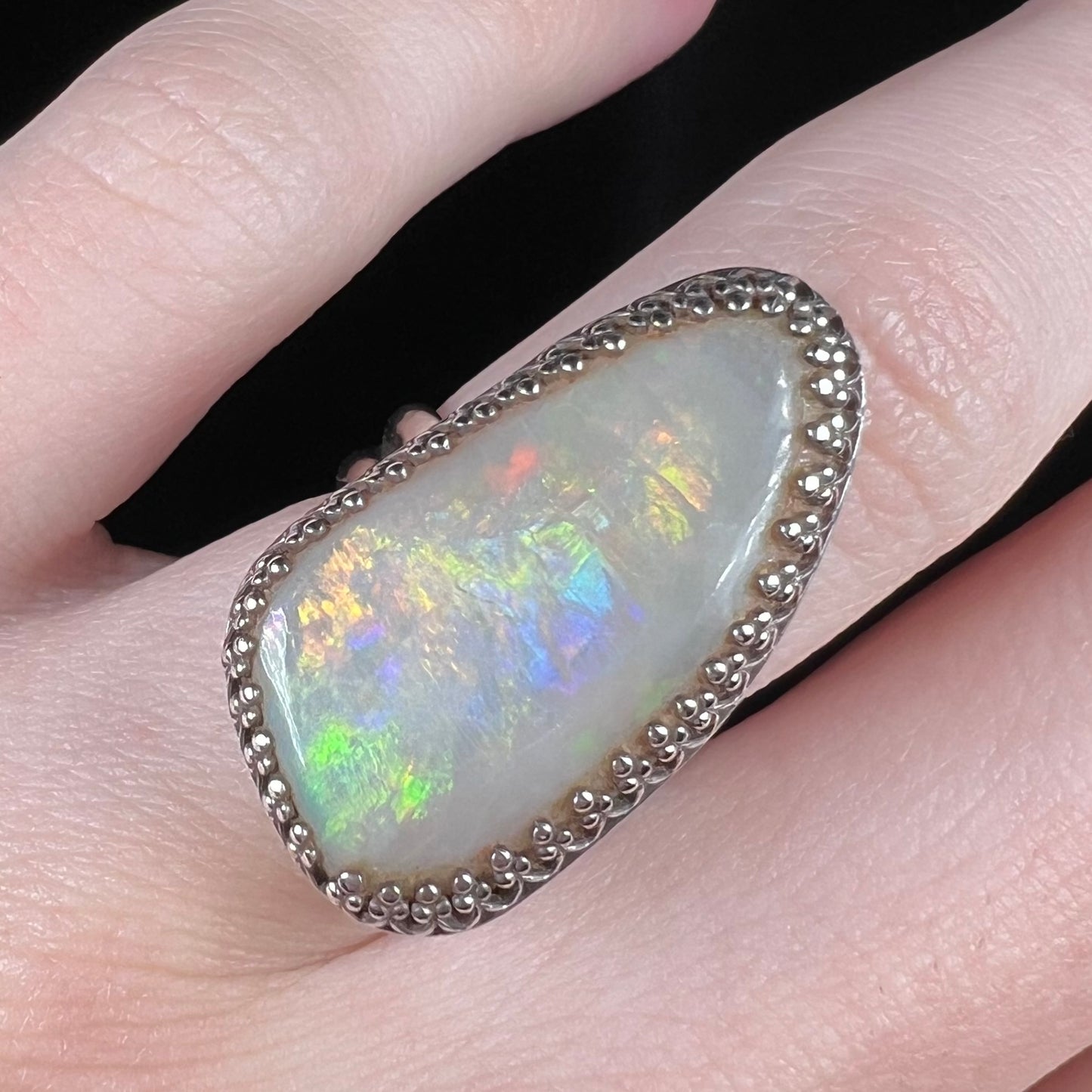 Close-up of a multicolor Coober Pedy, Australian opal ring worn on a hand.  The freeform-shaped opal has peacock-like colors under studio lighting.