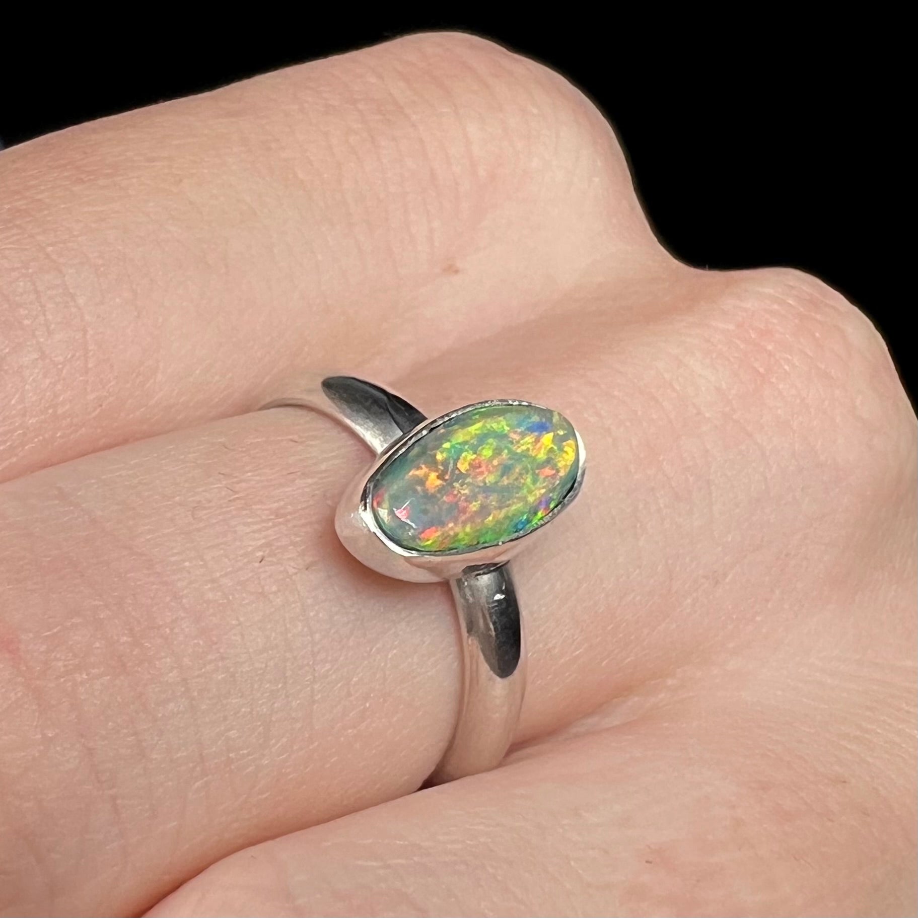 Angled view looking down a multicolor N5 dark Australian opal ring made from sterling silver, worn on a hand.