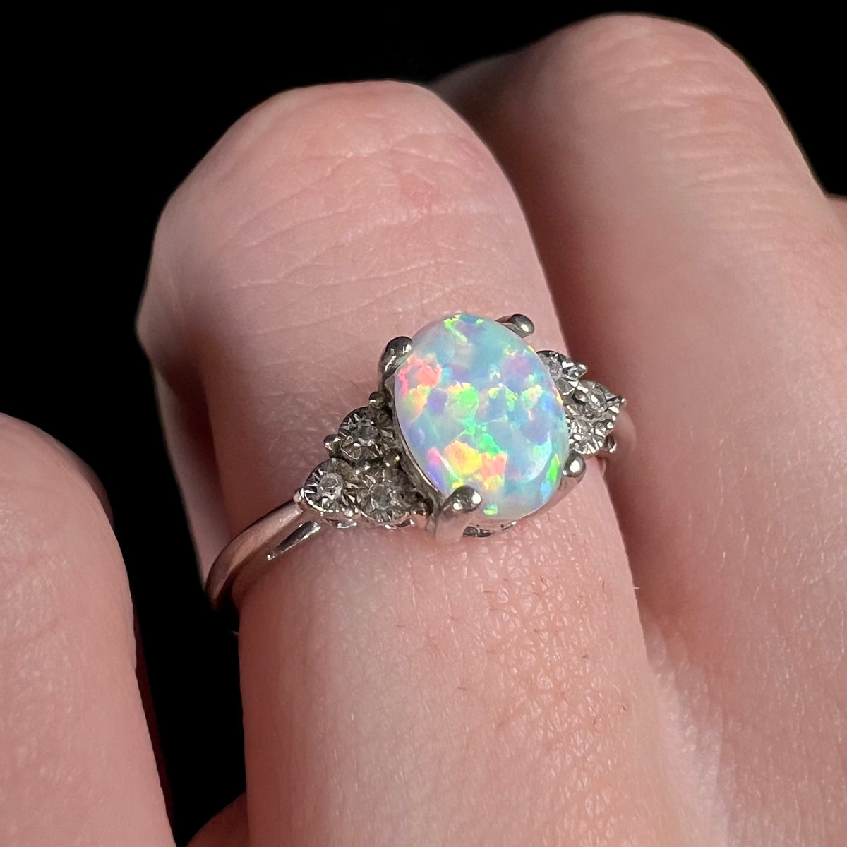 Multicolor flashes of color seen in sterling silver lab-created opal and diamond ring, worn on finger.