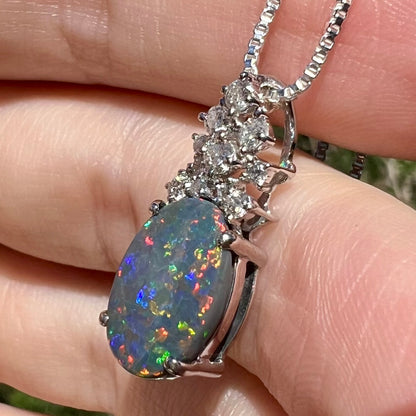 Side angle close-up of N3 black opal pendant with multicolor red and blue flashes, held in sunlight.