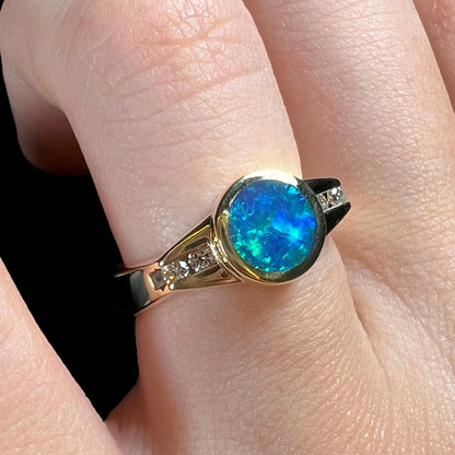 Angled close-up of a vintage boulder opal ring with an N4 black body tone, shown on a finger under studio lights.