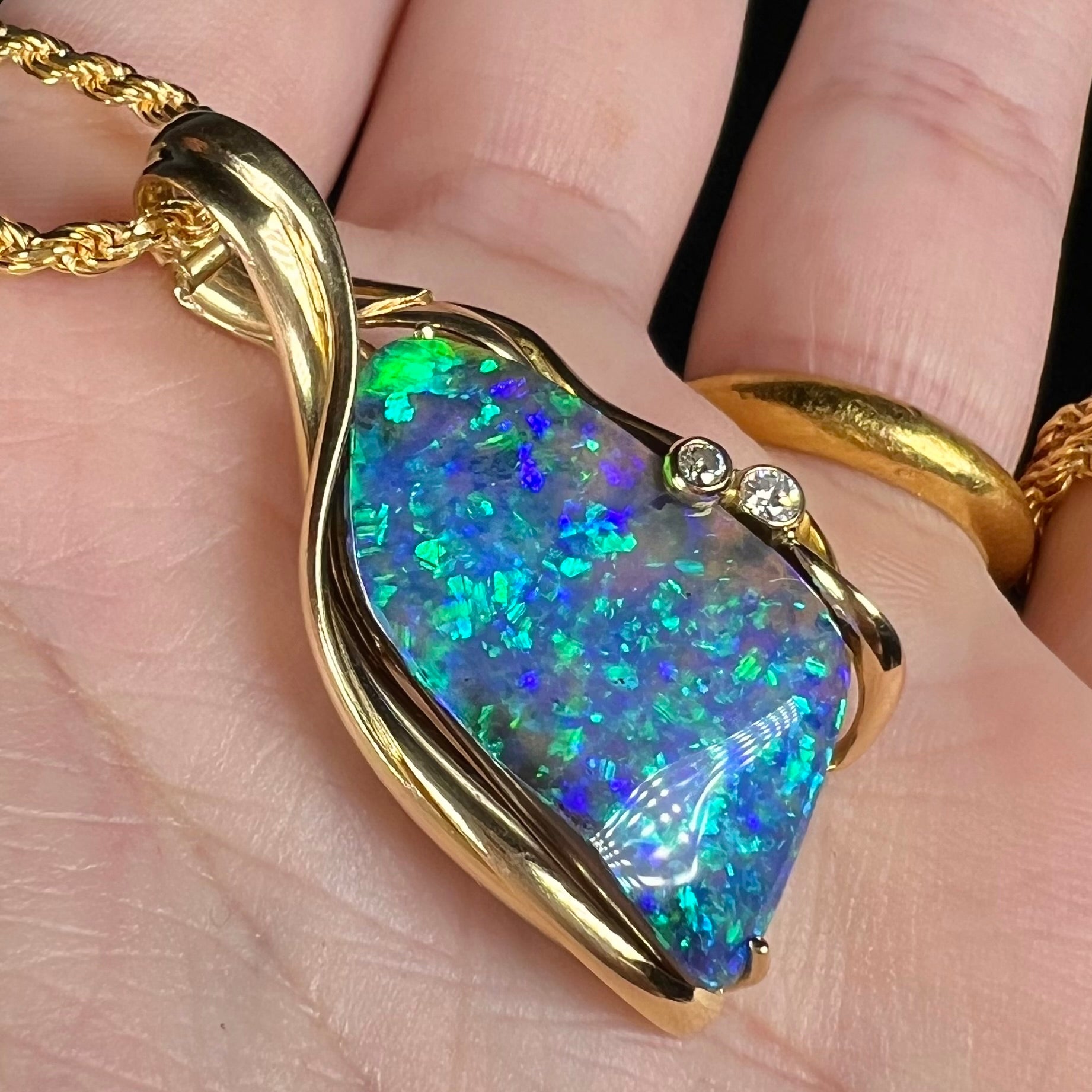 Yellow gold boulder opal pendant with dark N5 body tone shown close-up in hand from angle.